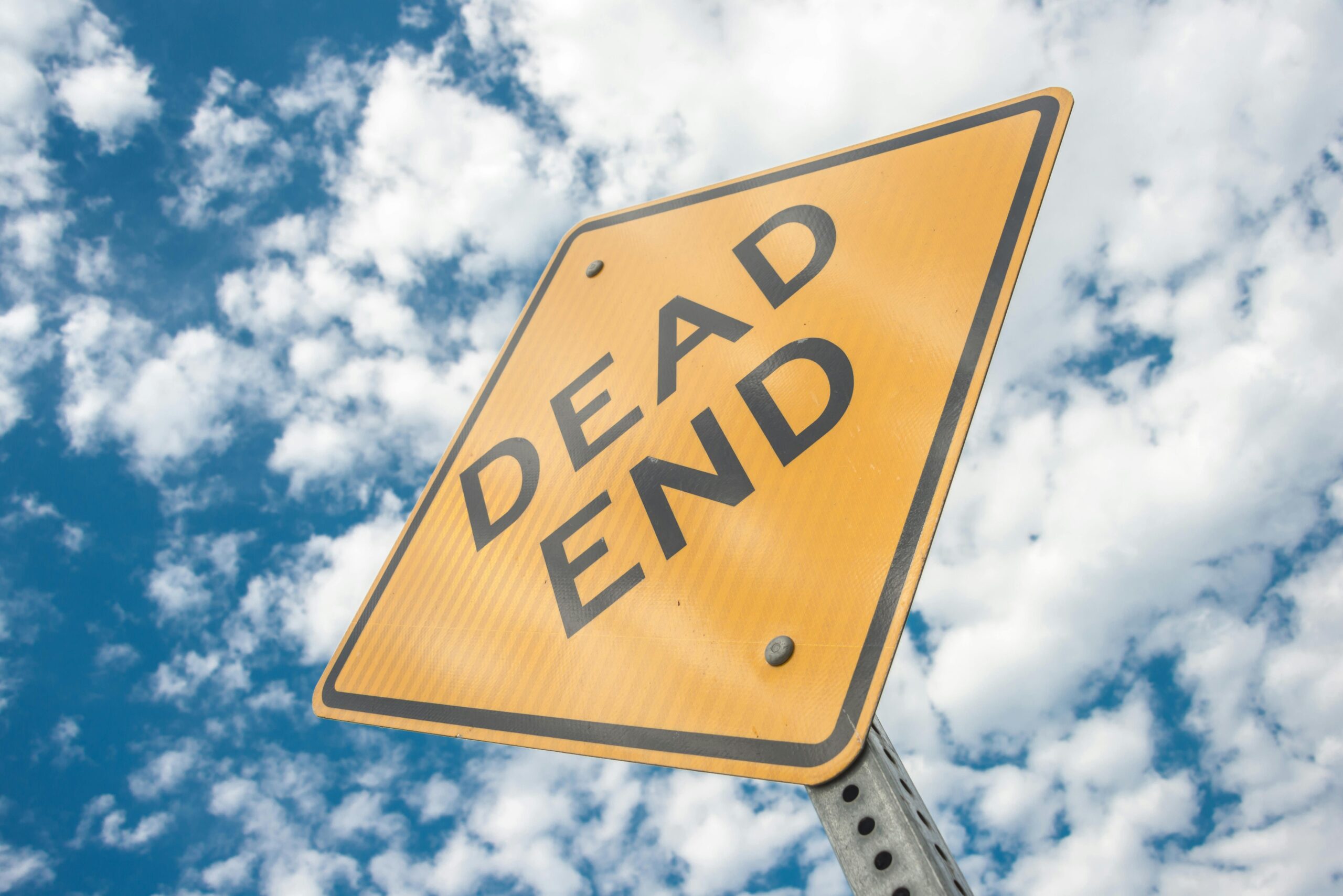 Close-up of a dead end road sign against a bright, cloudy blue sky, symbolizing restriction and caution.